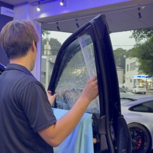 ドアガラスにカーフィルムを合わせて施工するスタッフ